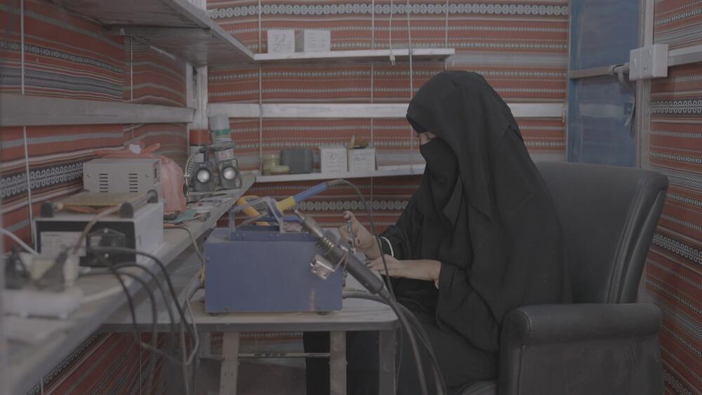  امرأة ترتدي نقابًا أسود وعباءة تجلس على مكتب وتحمل أدوات