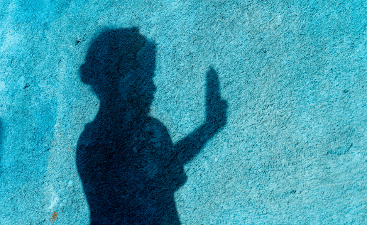 La sombra de una niña levanta la mano contra una pared azul