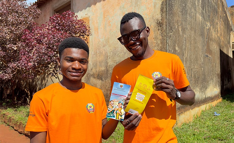 Two young men in orange tee-shirts hold up brochures.