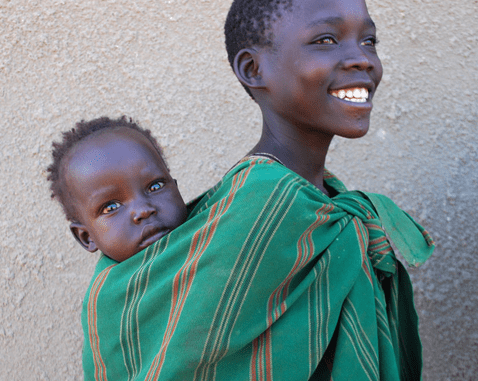 A teenager carries a baby on her back.